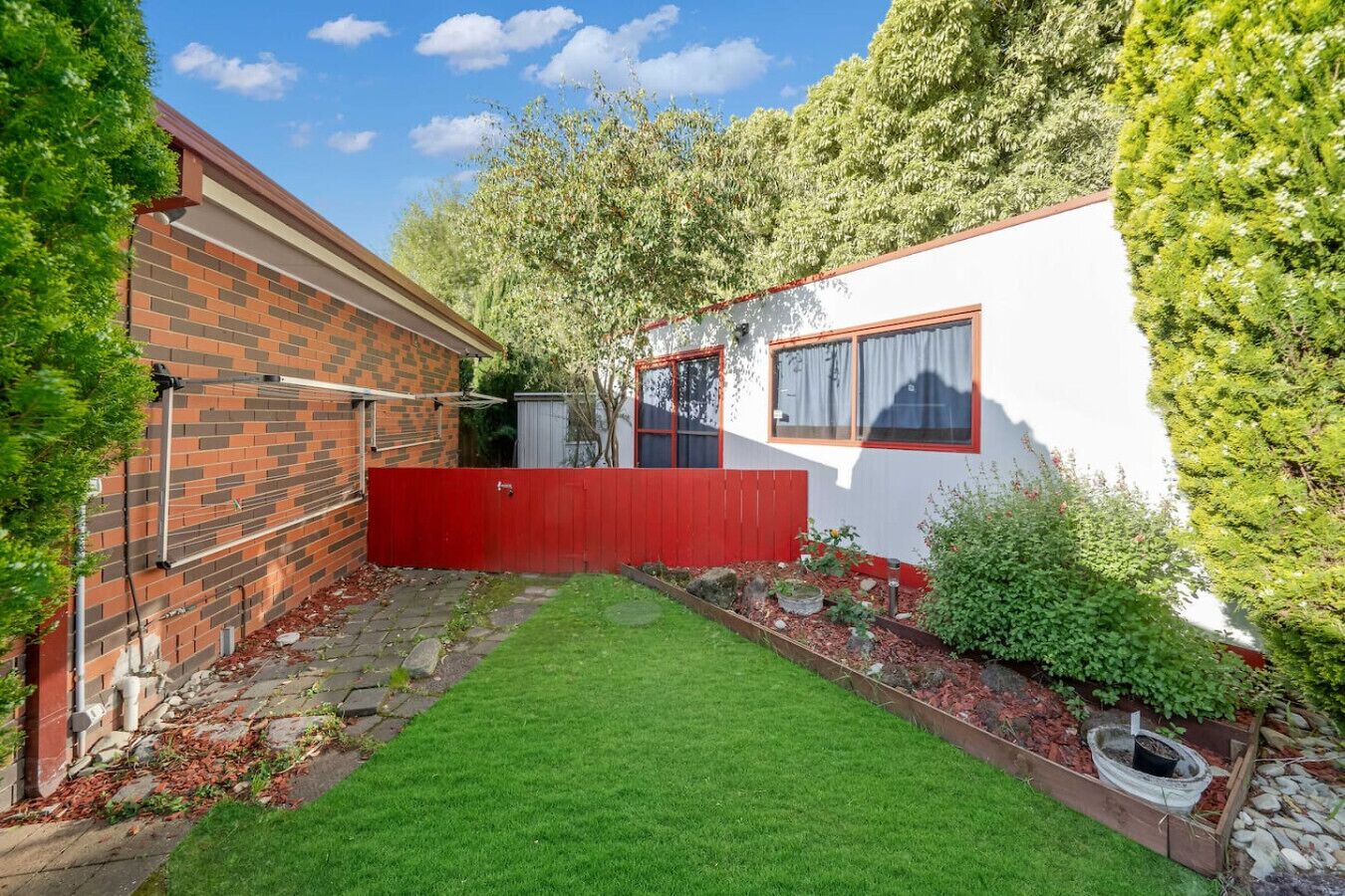 A residential property with a brick exterior, a red fence, a white wall, and a well-maintained lawn.