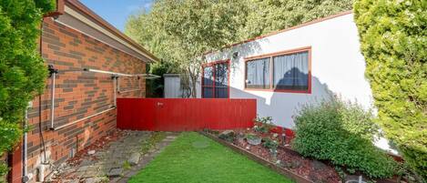 A residential property with a brick exterior, a red fence, a white wall, and a well-maintained lawn.