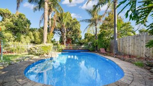 A round swimming pool with a stone border, surrounded by a wooden fence and palm trees. - FamParadise: Pool, Cabin, Garden, Peace & More ! (Berwick)