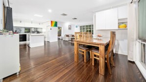 A modern kitchen with white cabinets, a wooden dining table, and a view of the living area. - FamParadise: Pool, Cabin, Garden, Peace & More ! (Berwick)