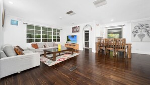 A modern living room with a sofa, coffee table, and dining area with chairs. - FamParadise: Pool, Cabin, Garden, Peace & More ! (Berwick)