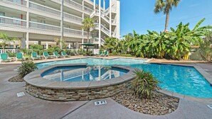 A hotel with a swimming pool surrounded by lounge chairs and palm trees.