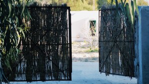 A rustic gate with a woven design, leading to a paved area with scattered pebbles. - Bangalow Chebba (LA CHEBBA)