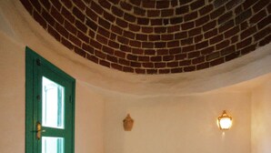 A room with a brick ceiling, a green door, a bed with multiple pillows, and two wall-mounted lights. - Bangalow Chebba (LA CHEBBA)