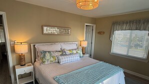 Une chambre à coucher avec un grand lit, deux tables de chevet avec des lampes, un luminaire au plafond, une fenêtre avec des stores et une porte.