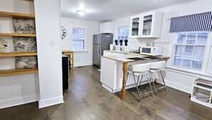 A modern kitchen with white cabinets, a stainless steel refrigerator, a microwave, and a wooden island with bar stools.