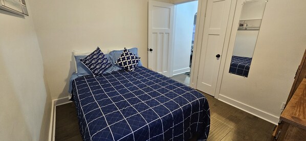 Un dormitorio con cama, dos almohadas, una puerta, un espejo y un mueble de madera.