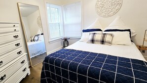 A bedroom with a bed, dresser, mirror, and window with blinds.