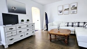 A living room with a white sofa, a wooden coffee table, a white dresser with multiple drawers, a flat-screen TV, and framed pictures on the wall.