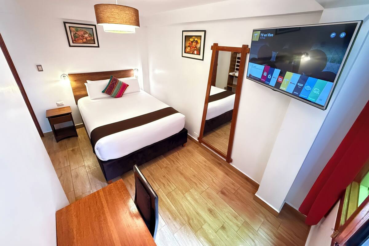 Een moderne hotelkamer met een bed, nachtkastje, televisie en een spiegel.