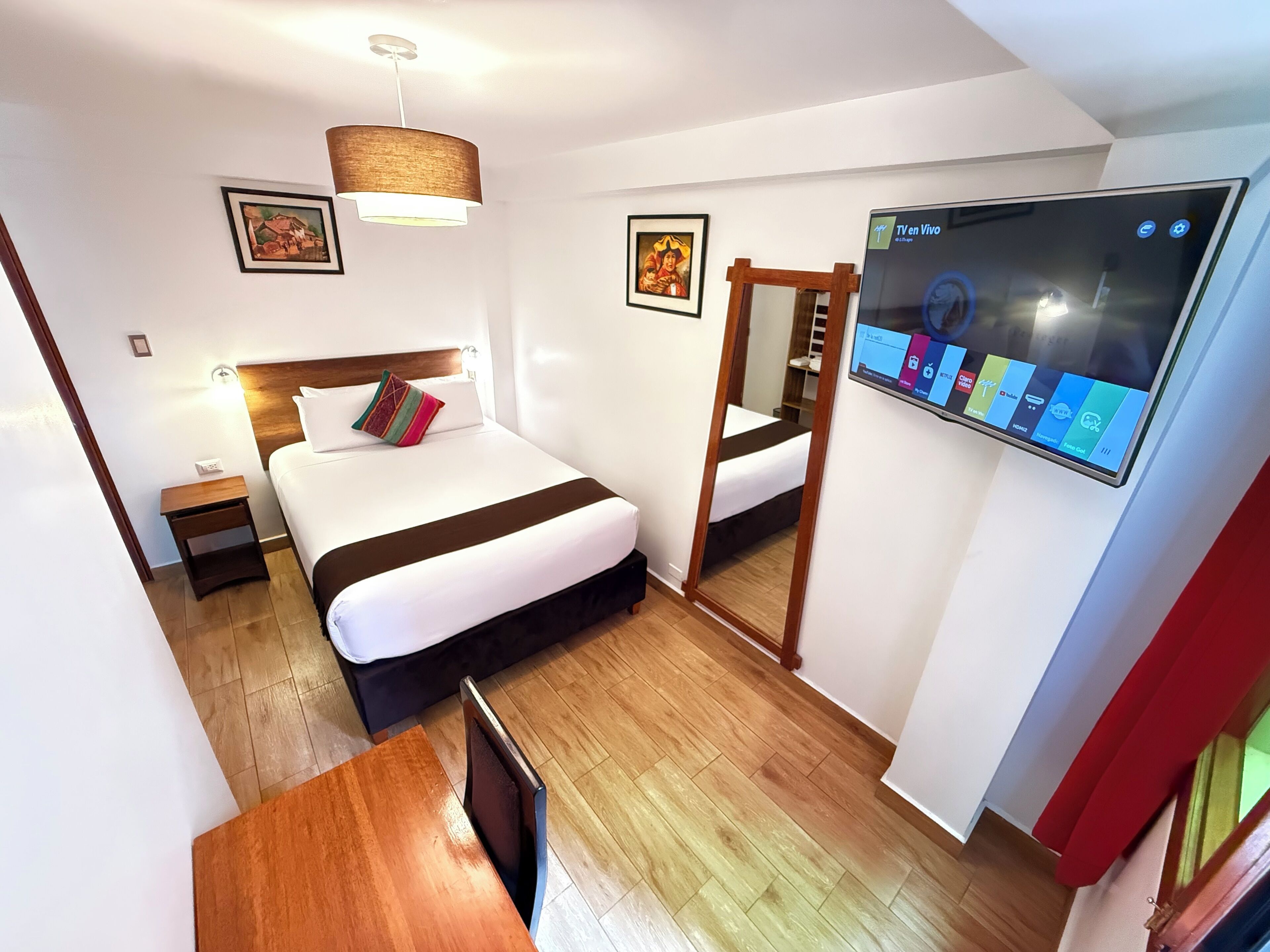 Une chambre d’hôtel avec un lit, une table de chevet, une lampe, une télévision et un plancher en bois.