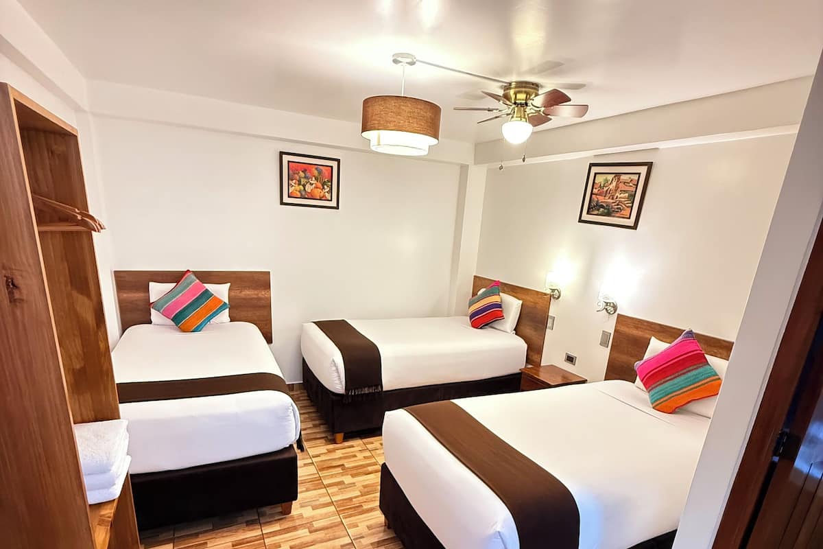 Een hotelkamer met drie bedden, houten vloeren en een plafondventilator.