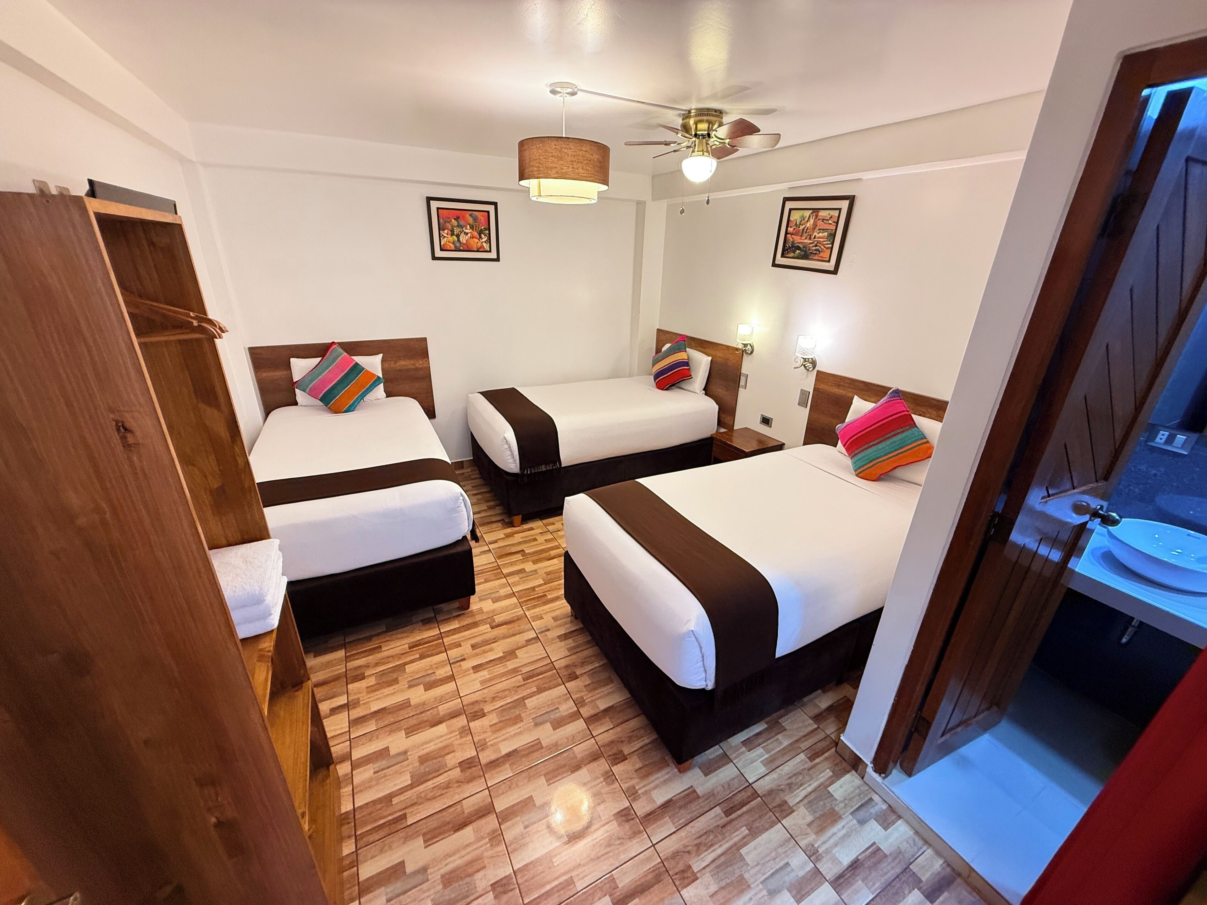 A hotel room with two beds, a wooden wardrobe, a ceiling fan, and two wall-mounted light fixtures.