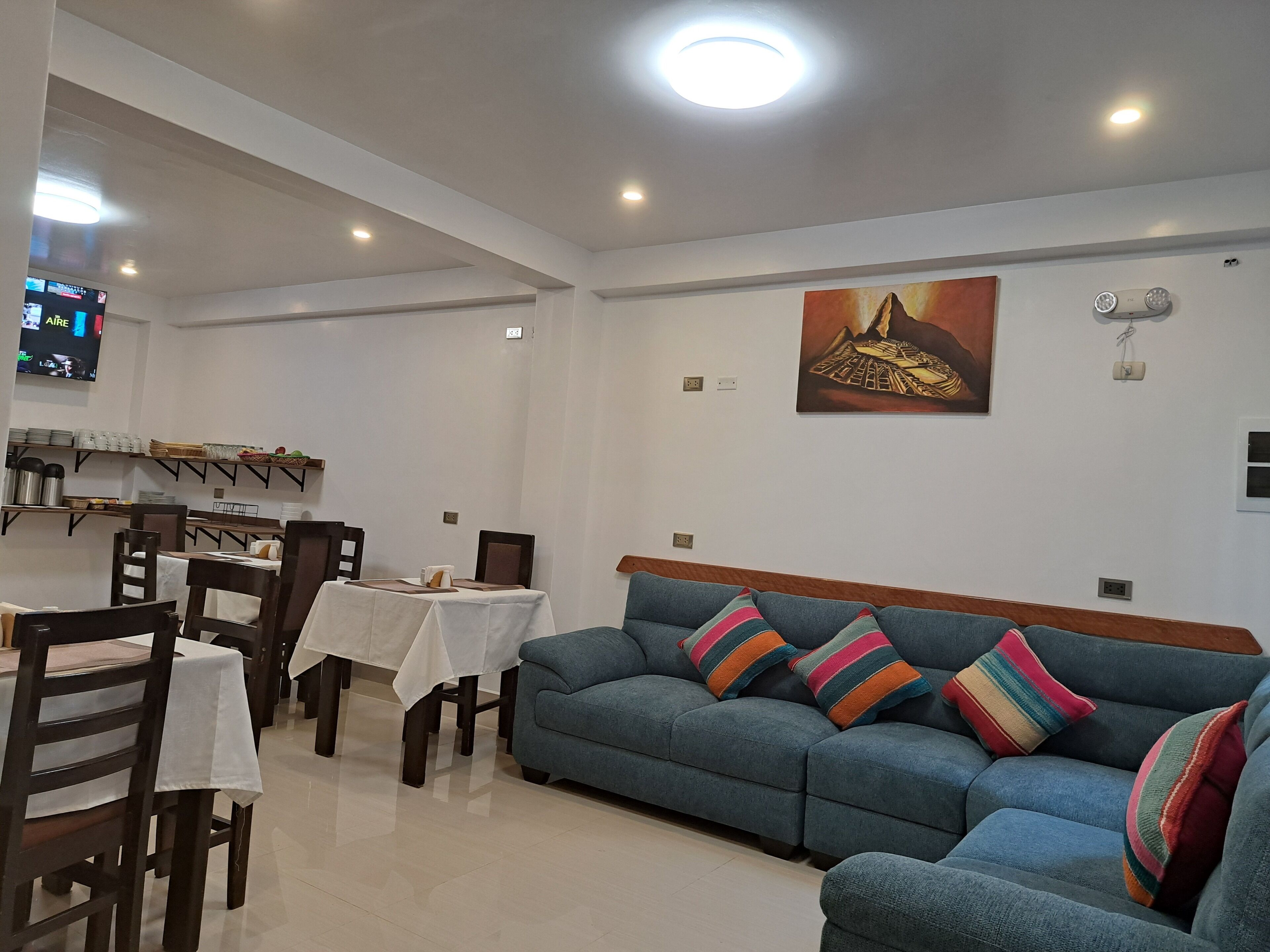 A dining area with a table set for two, a blue sofa with colorful cushions, and a painting on the wall.