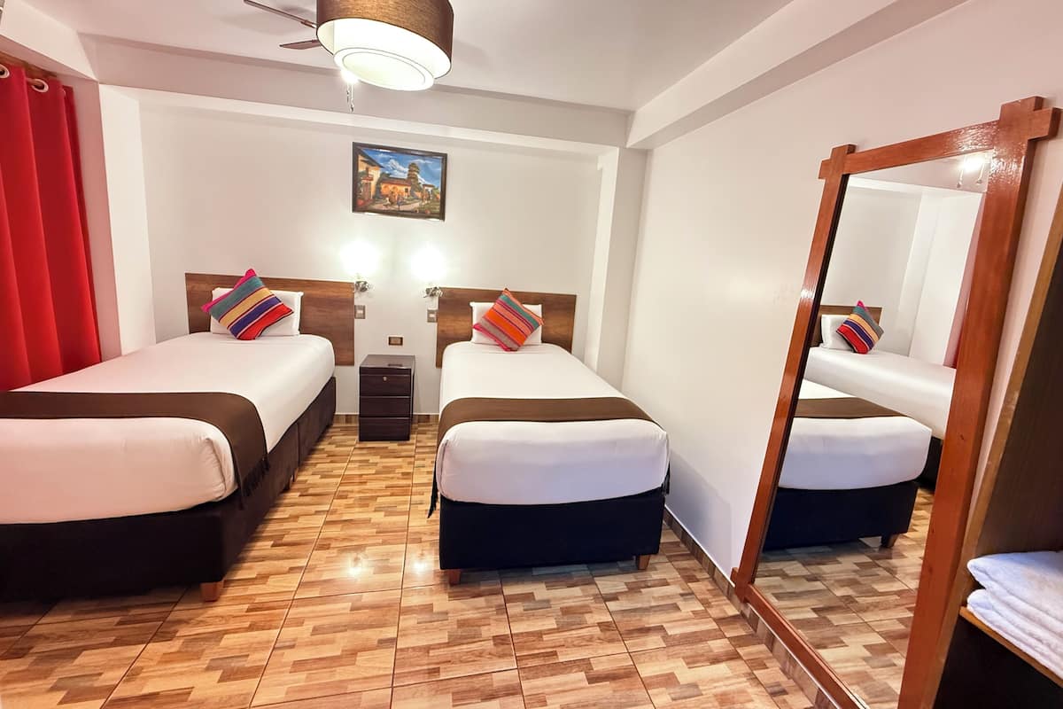 Hotelkamer met twee bedden, houten vloer, plafondventilator, spiegel en een schilderij aan de muur.