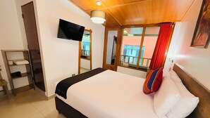 A hotel room with a bed, a TV, a wooden ceiling, a window with a view, and a shelf with towels. - Inti Pacha Palace Machupicchu (Machu Picchu)
