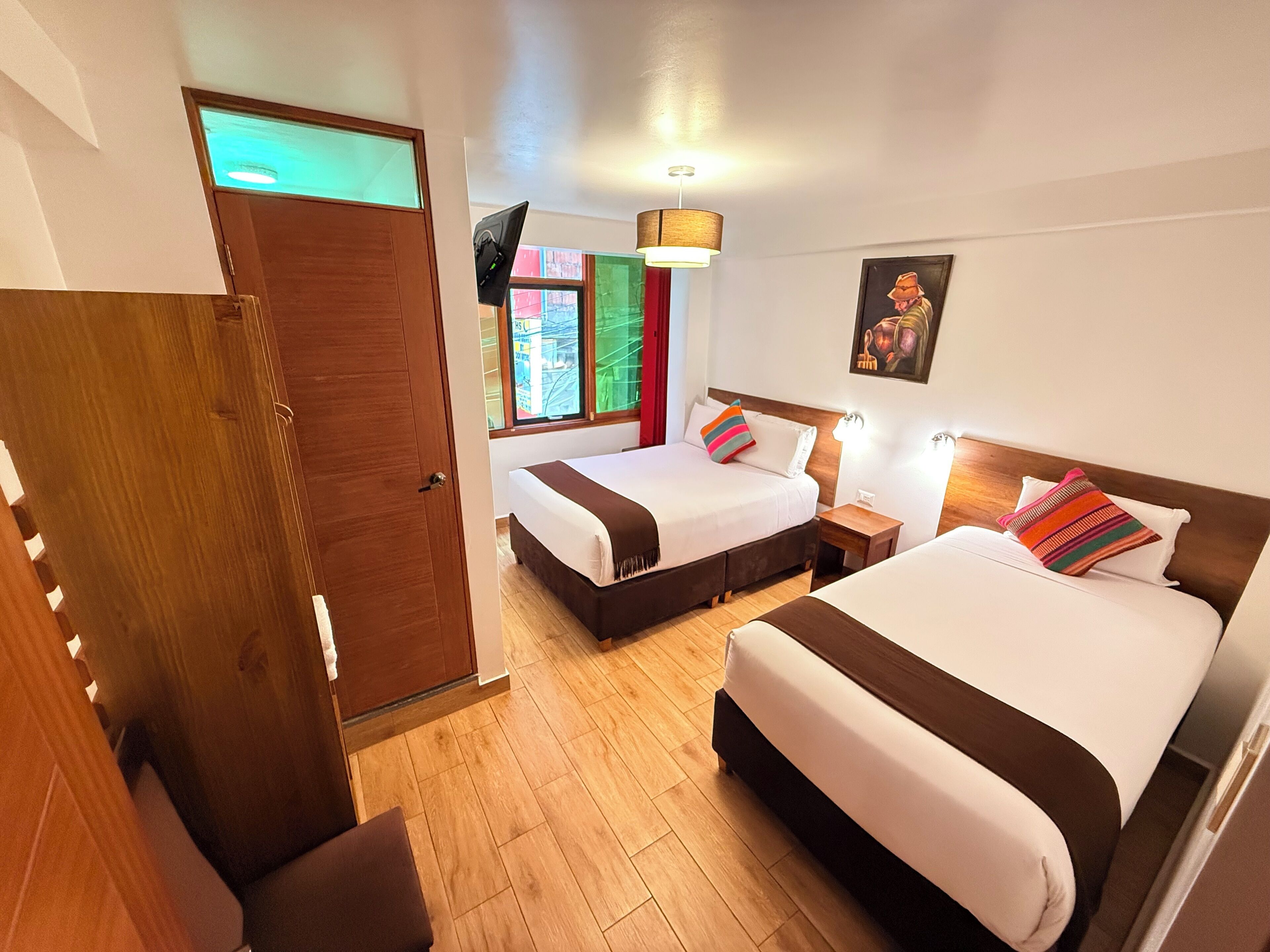 Habitación de hotel con dos camas, suelo de madera, televisión y un cuadro en la pared.