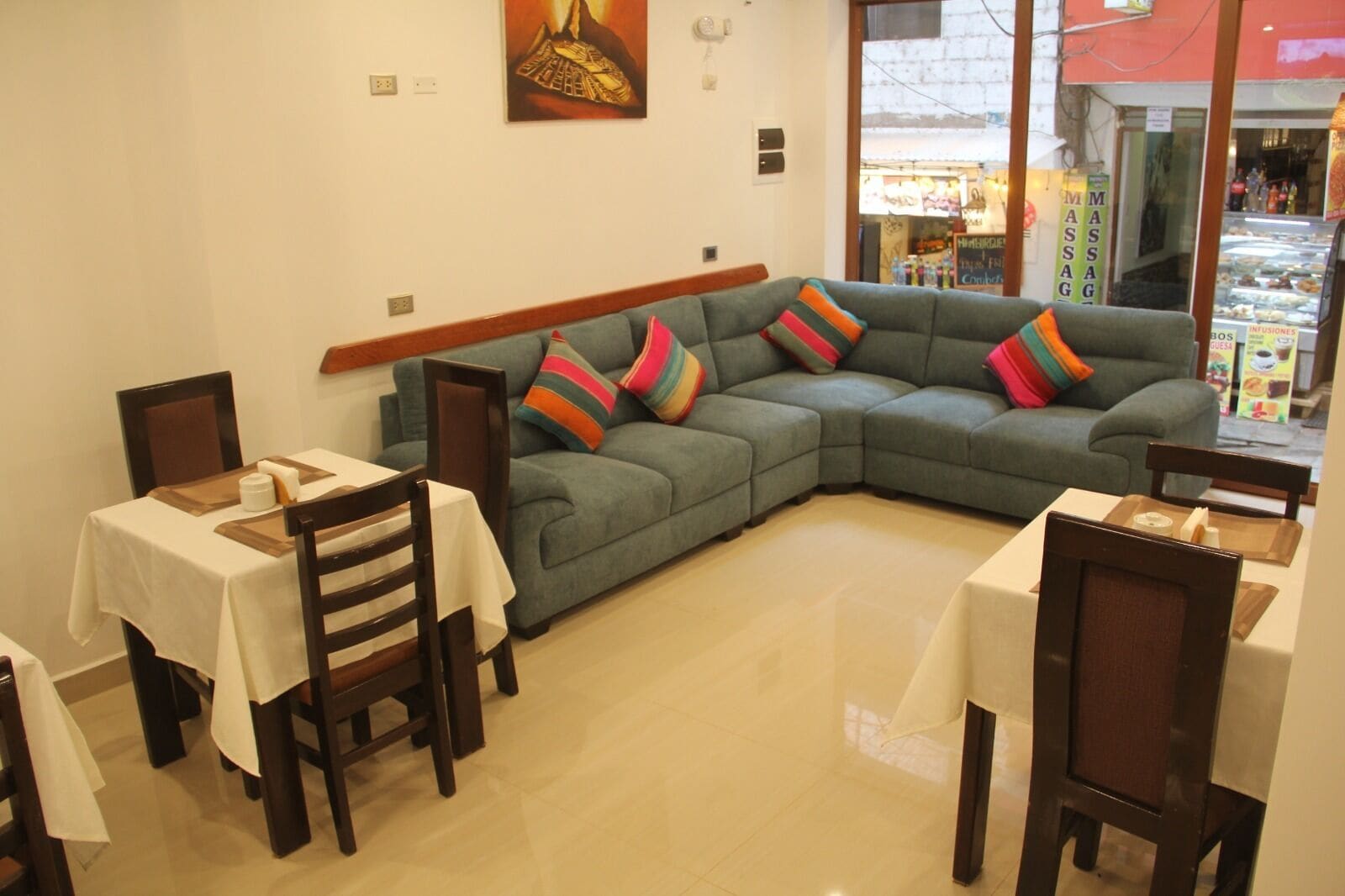 A dining area with a green sofa and two tables, one with a white tablecloth and another with a brown tablecloth.