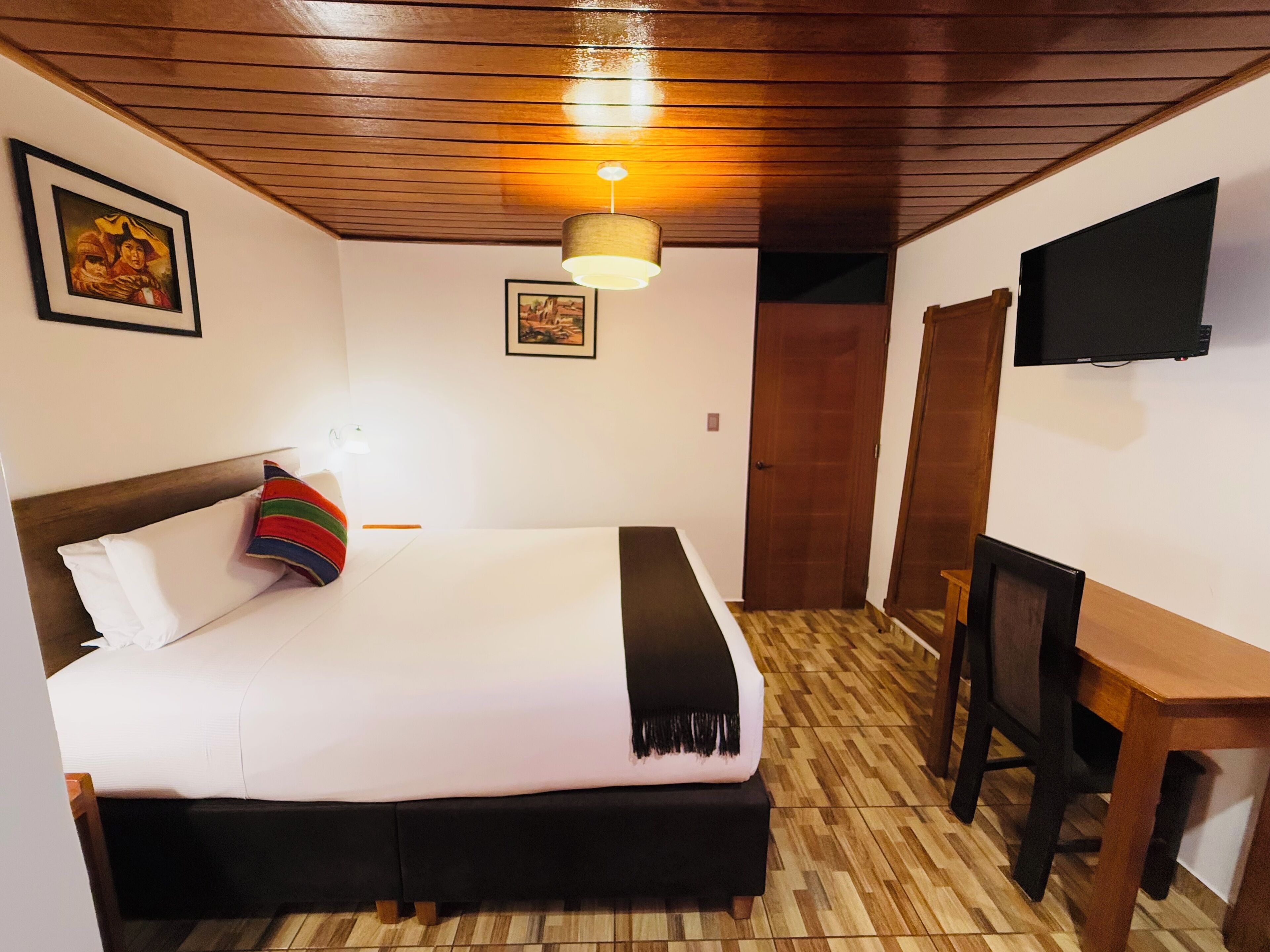A hotel room with a bed, a desk, a television, and wooden flooring.