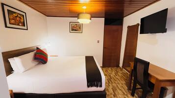 A hotel room with a bed, a desk, a television, and wooden flooring.