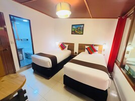 Une chambre d’hôtel avec deux lits, une table en bois, une salle de bain visible à travers une porte en verre et un tableau accroché au mur.