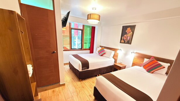 A hotel room with two beds, wooden flooring, a painting on the wall, and a window with colorful curtains. - Inti Pacha Palace Machupicchu (Machu Picchu)