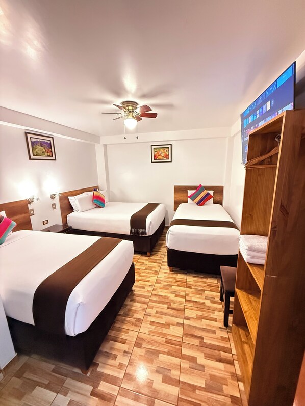 A hotel room with three beds, a ceiling fan, wooden flooring, and a wardrobe.