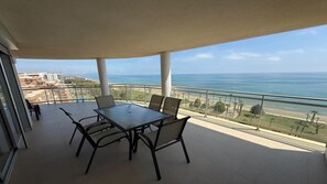 A balcony with a table and chairs, overlooking a beach and ocean.