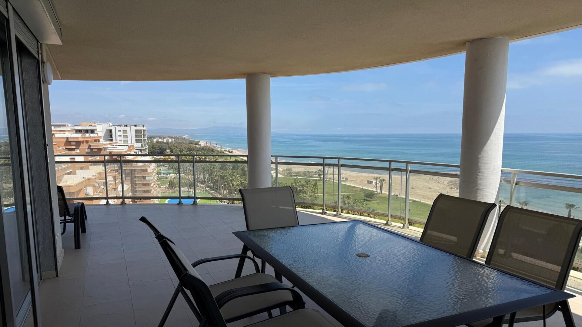 A balcony with a table and chairs, overlooking a beach and ocean.