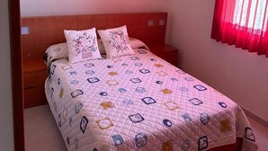Une chambre à coucher avec un lit, une tête de lit en bois, un rideau rouge et un tableau accroché au mur.
