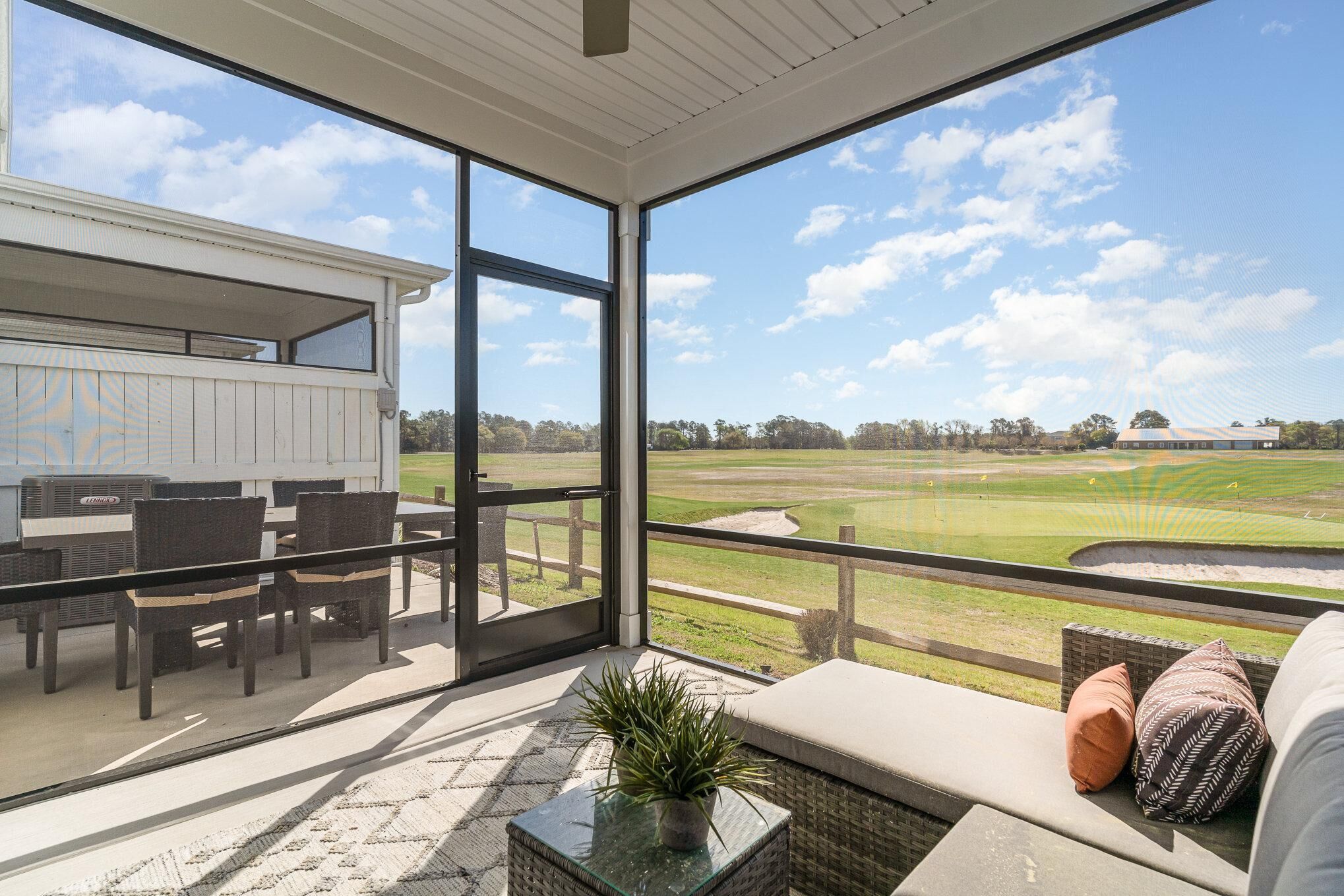 A balcony with a view of a golf course, wicker furniture, and a potted plant.