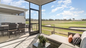 A balcony with a view of a golf course, wicker furniture, and a potted plant.