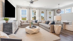 A modern living room with a sectional sofa, a coffee table, and a flat-screen TV mounted on the wall.