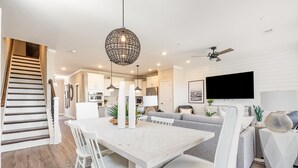 A modern kitchen with white cabinets, a dining area with a white table and chairs, and a staircase with wooden steps.