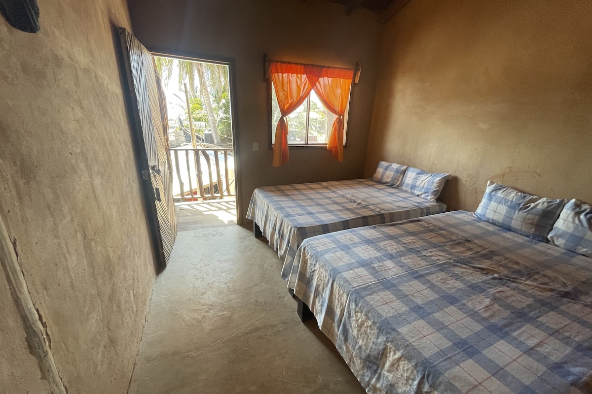 Une chambre avec deux lits, une fenêtre avec des rideaux orange et une vue sur des palmiers à l’extérieur.
