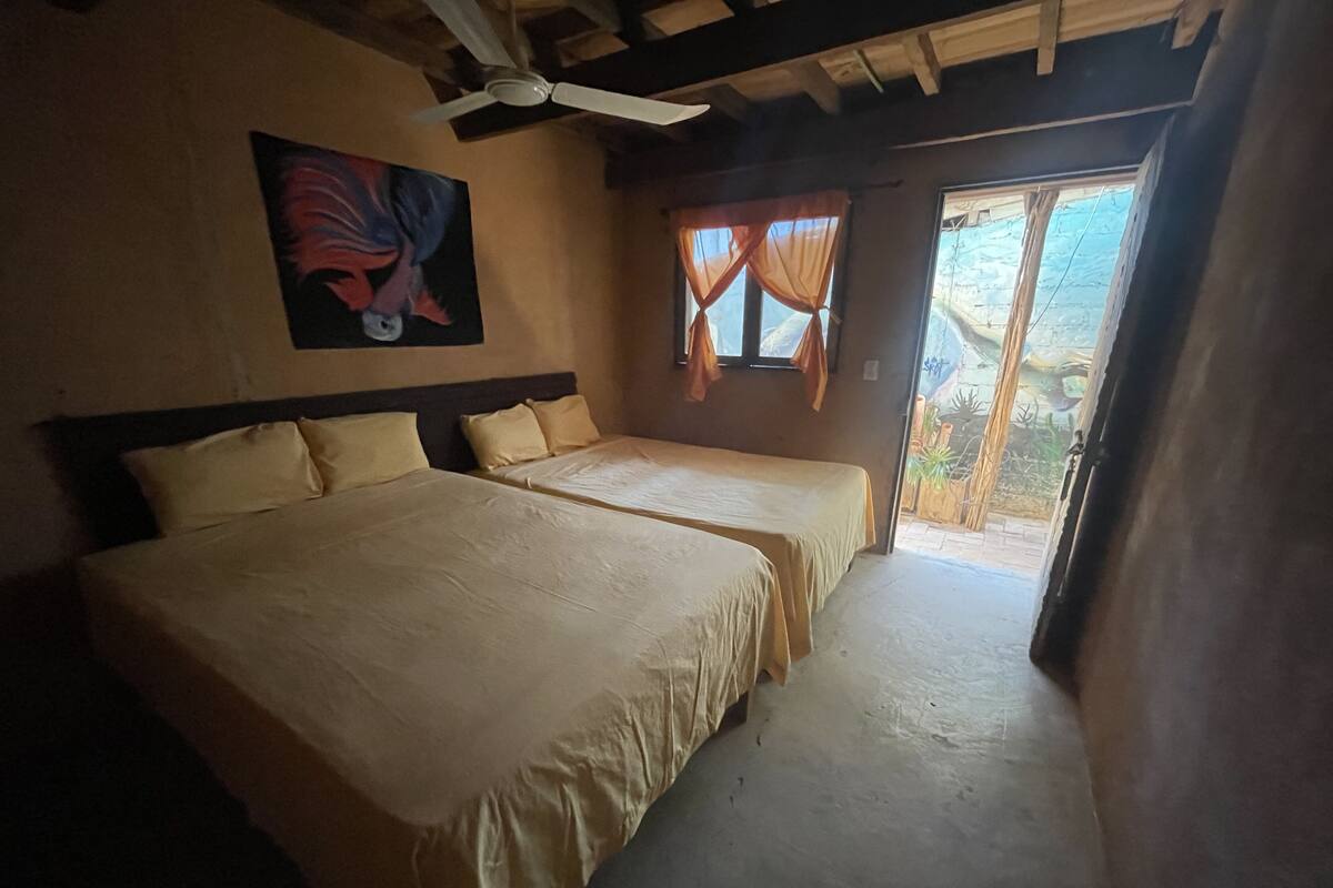 Une chambre avec deux lits, un ventilateur de plafond, un tableau et une fenêtre avec des rideaux.