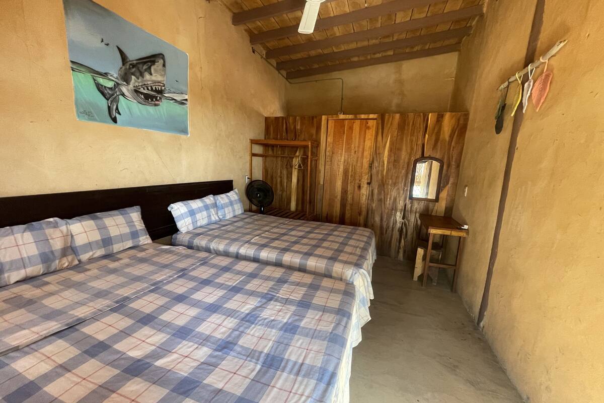 Une chambre avec deux lits, un plafond en bois, un ventilateur et un tableau représentant un requin.