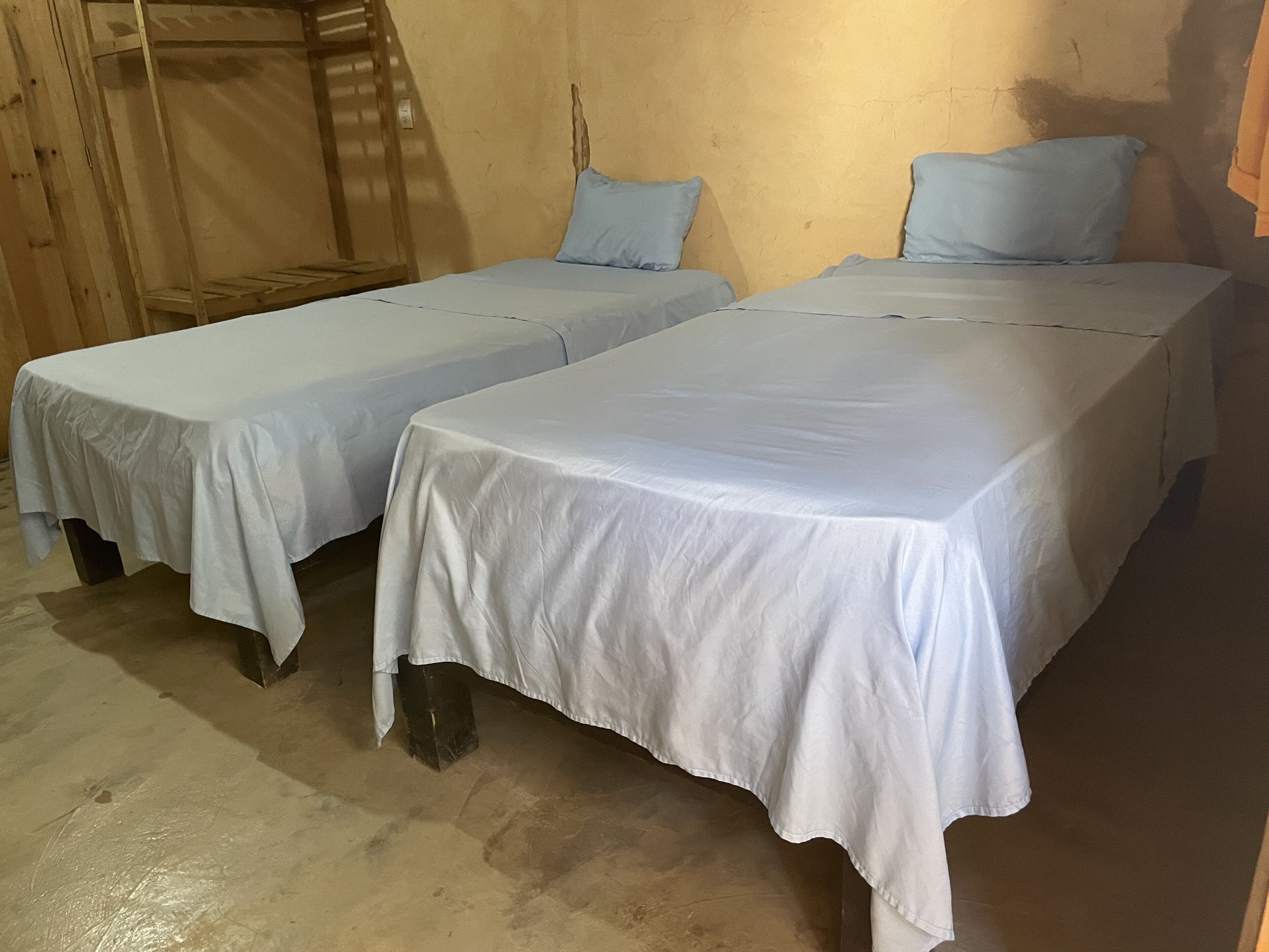 Deux lits simples avec du linge de lit blanc, des têtes de lit en bois et un lit superposé avec une échelle en bois.