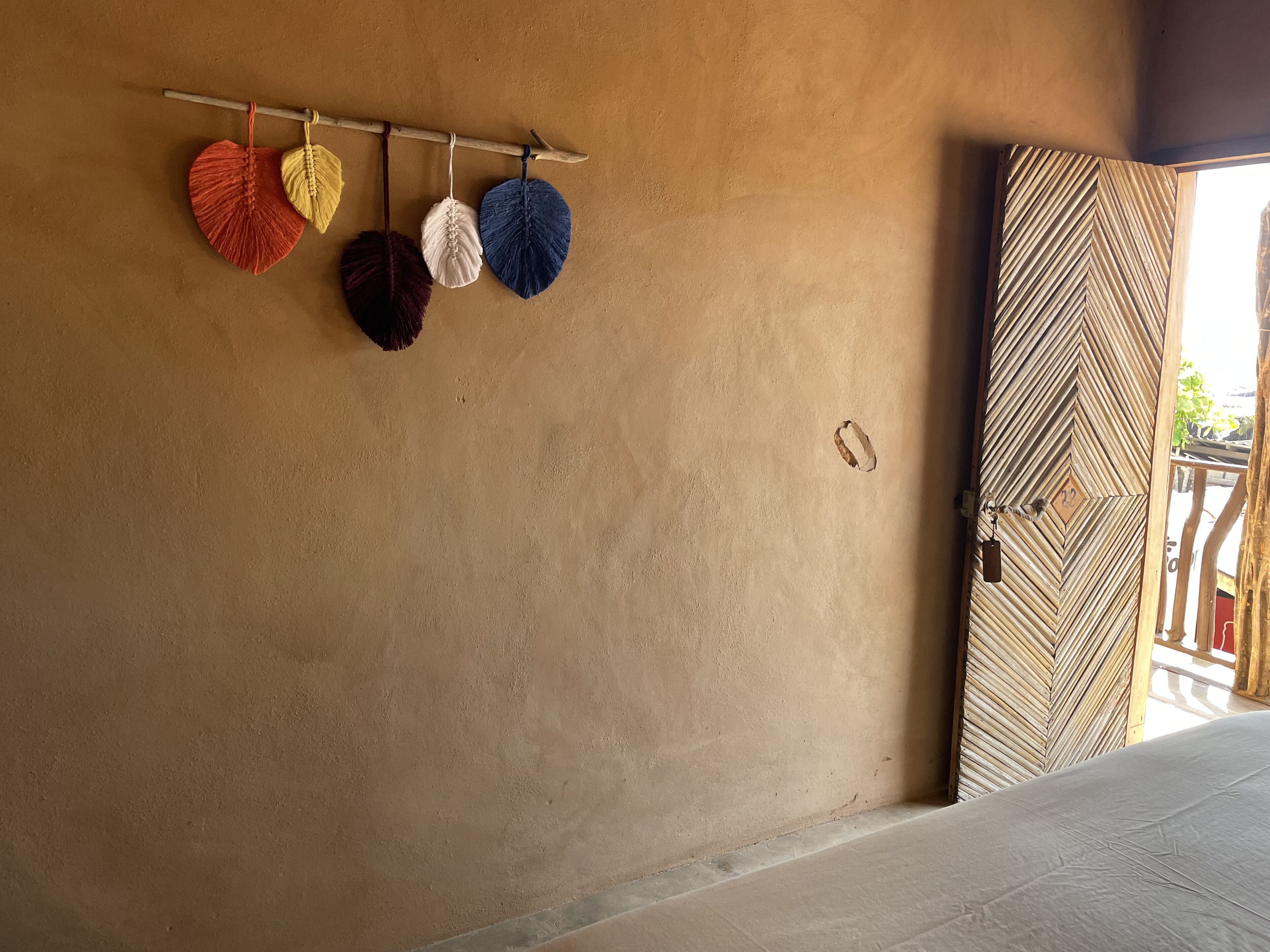 Una stanza con una parete strutturata, una porta in legno decorata con un motivo geometrico e un letto con lenzuolo bianco.