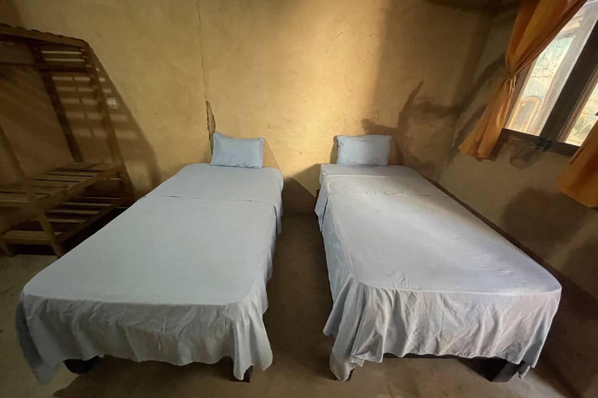 Une chambre avec deux lits simples, un escalier en bois et une fenêtre avec des rideaux.