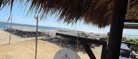 Vista de la playa con una estructura de techo de paja y un letrero que dice 'OKANSI Cabaña'.