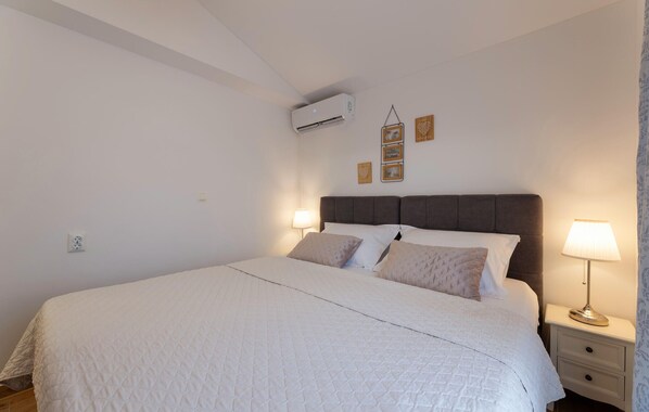 A neatly made bed with a quilted white duvet, a dark headboard, and two bedside lamps.
