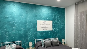 A bedroom with teal walls, two beds, and a quote plaque. - Tutta nata storia (Naples)