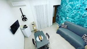 A living room with a sofa, a dining table with chairs, a guitar, a TV, and a large window with curtains. - Tutta nata storia (Naples)
