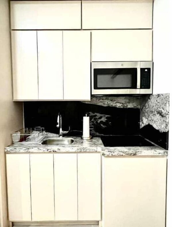 Cocina compacta con armarios blancos, microondas, pileta de cocina y encimera de mármol.