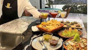 Uno chef in cucina, con un grande tavolo da pranzo apparecchiato per un pasto, con vista sulla città.