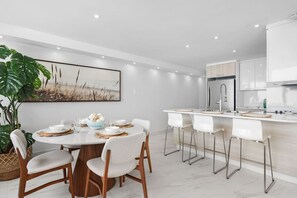 Une cuisine moderne avec des meubles blancs, un coin repas doté d’une table ronde et de chaises, et un grand tableau accroché au mur.