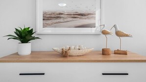A framed seascape artwork, a potted plant, a decorative bowl with eggs, and two bird sculptures on a wooden shelf. - Beachfront Sanctuary Newly Renovated to Perfection with Full Power Generator (Carolina)