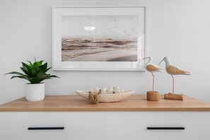 A framed seascape artwork, a potted plant, a decorative bowl with eggs, and two bird sculptures on a wooden shelf. - Beachfront Sanctuary Newly Renovated to Perfection with Full Power Generator (Carolina)