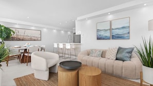 A modern living room with a beige sofa, a dining area with a white table, and a kitchen with white bar stools. - Beachfront Sanctuary Newly Renovated to Perfection with Full Power Generator (Carolina)